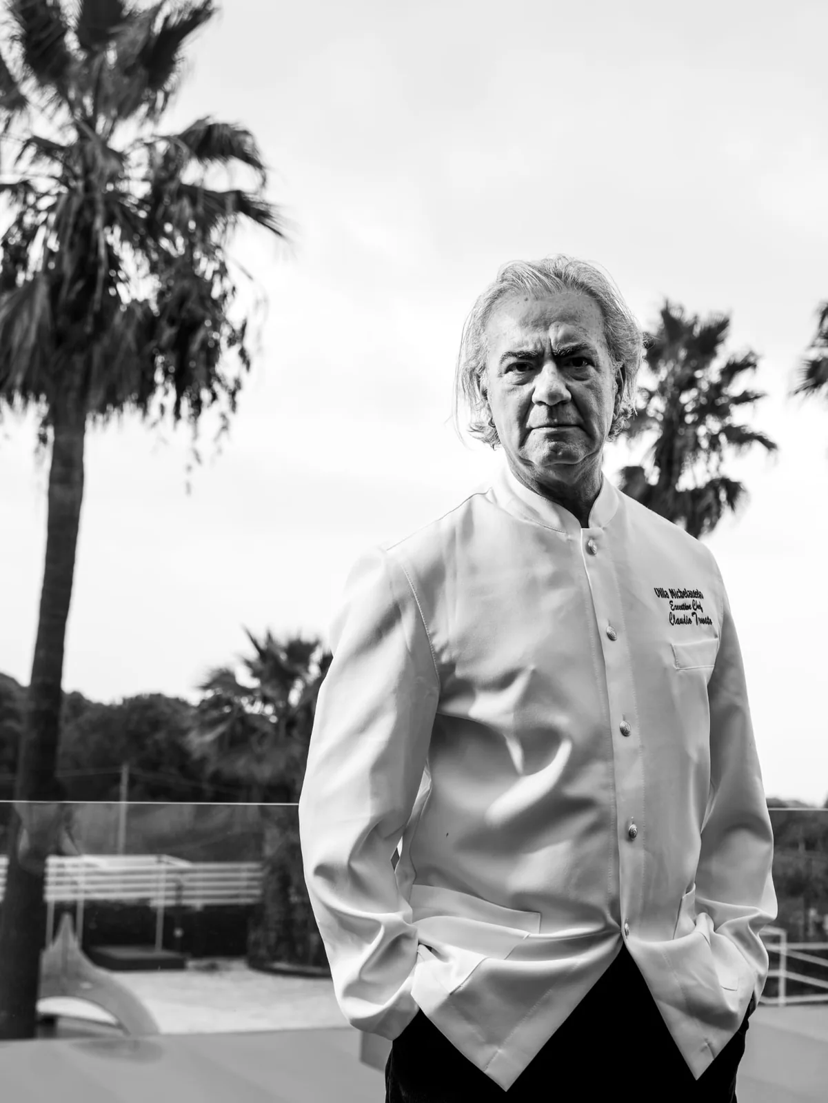 Lo chef in giacca bianca, mani in tasca, fra le palme di Villa Michelangelo. Bianco e nero.