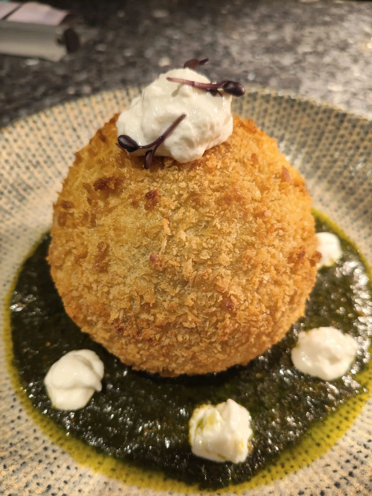 Arancino siciliano dorato adagiato su una crema al basilico.