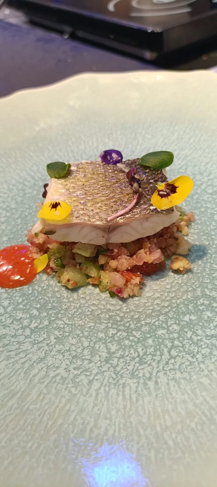 Filetto di pesce dalla pelle croccante su tabulé agli agrumi con fiori eduli.