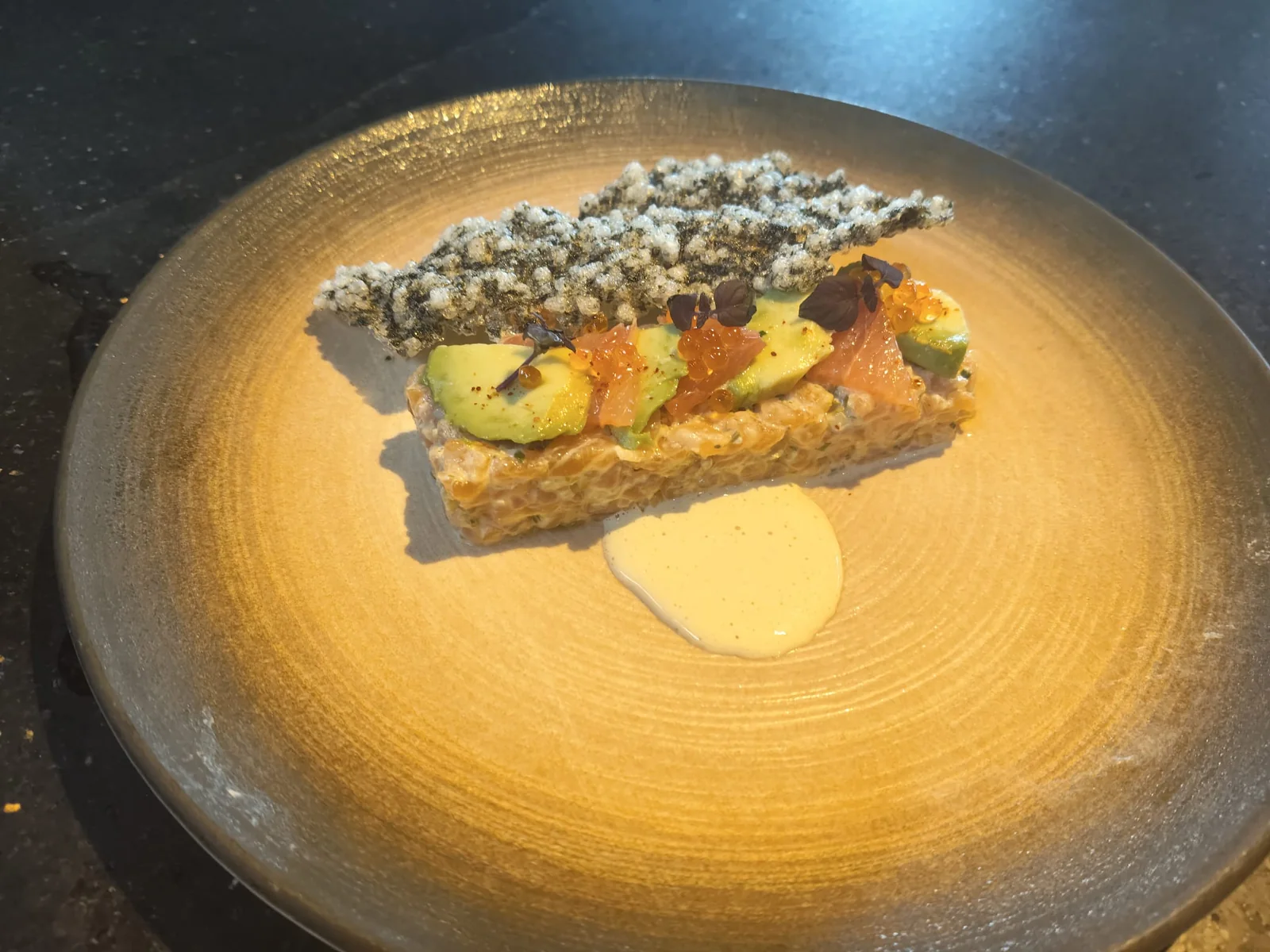 Battuta di salmone e avocado a strati con cialda croccante su piatto dorato.